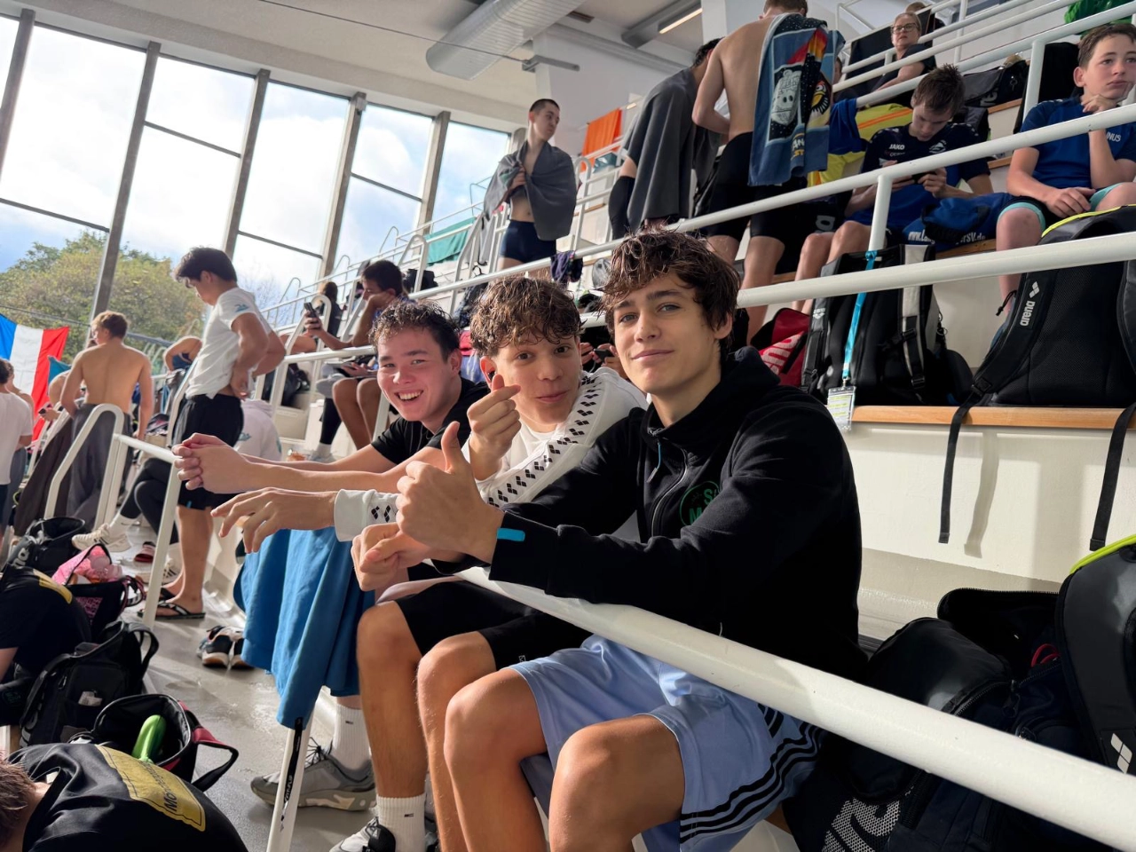 SGMG-Teamgeist bei den Bezirksmeisterschaften 2026 Drei junge Schwimmer der SG Mönchengladbach sitzen gut gelaunt auf der Tribüne der Schwimmoper Wuppertal
